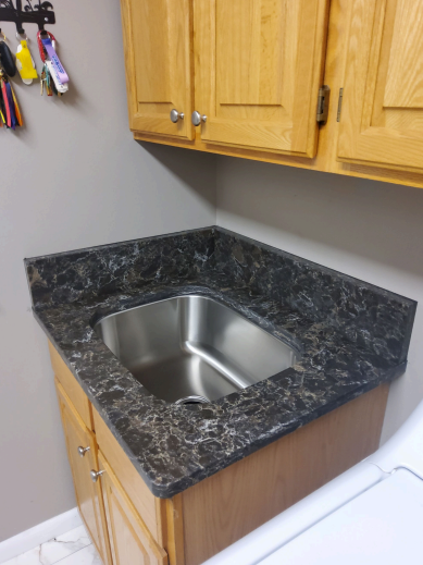 Laundry room countertop with dark quartz featuring a built-in stainless steel sink and oak cabinetry.