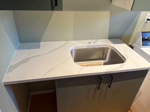 Laundry room countertop with light quartz featuring subtle veining, a built-in stainless steel sink, and modern cabinetry.