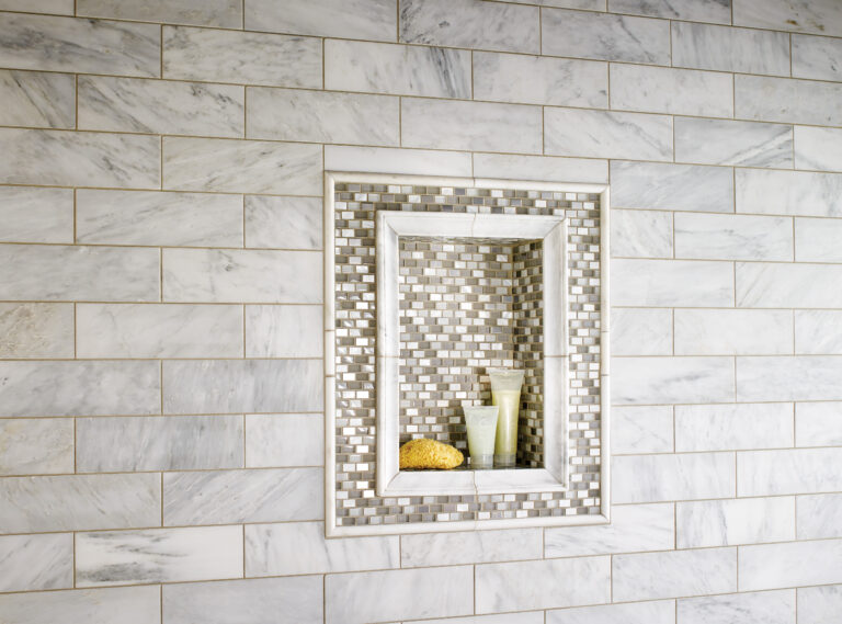 White and gray marble subway tile shower wall with a recessed niche framed in glass mosaic tile