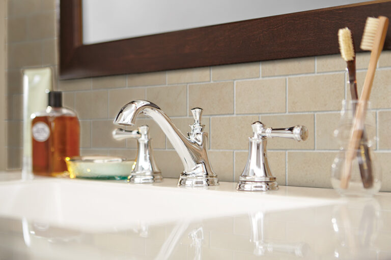 Polished chrome bathroom faucet on a white vanity top with a beige subway tile backsplash