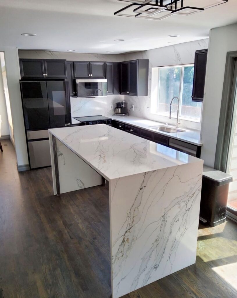 White quartz waterfall kitchen island with gold and gray veining, dark cabinets and full slab backsplash
