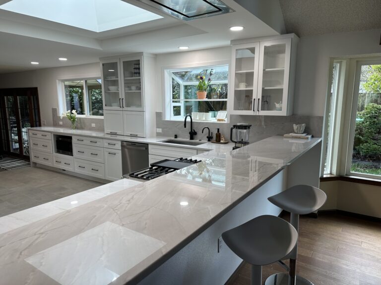 White and gray quartzite kitchen peninsula with gas cooktop, bar stools and white cabinets