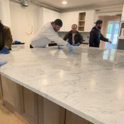 Tops Countertops team applying sealant to a newly installed marble kitchen island to protect the surface from stains and moisture.
